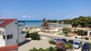 A coastal view with a beach, a parking area, and a building with a red roof. - Beachfront Apartment Mareo 6 (Nin)