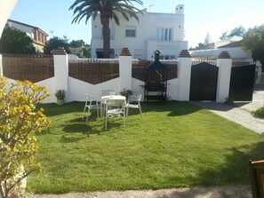 Ein gepflegter Rasen mit einer Terrassenfläche, einem weißen Zaun und einem modernen Gebäude im Hintergrund.