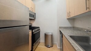 A compact kitchen with stainless steel appliances, a microwave, a trash bin, and a granite countertop. - Stunning 1-bedroom apartment in Financial District with Incredible Views! (New York)