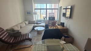 A modern living room with a sofa, a glass coffee table, a leather chair, and a television. - Stunning 1-bedroom apartment in Financial District with Incredible Views! (New York)