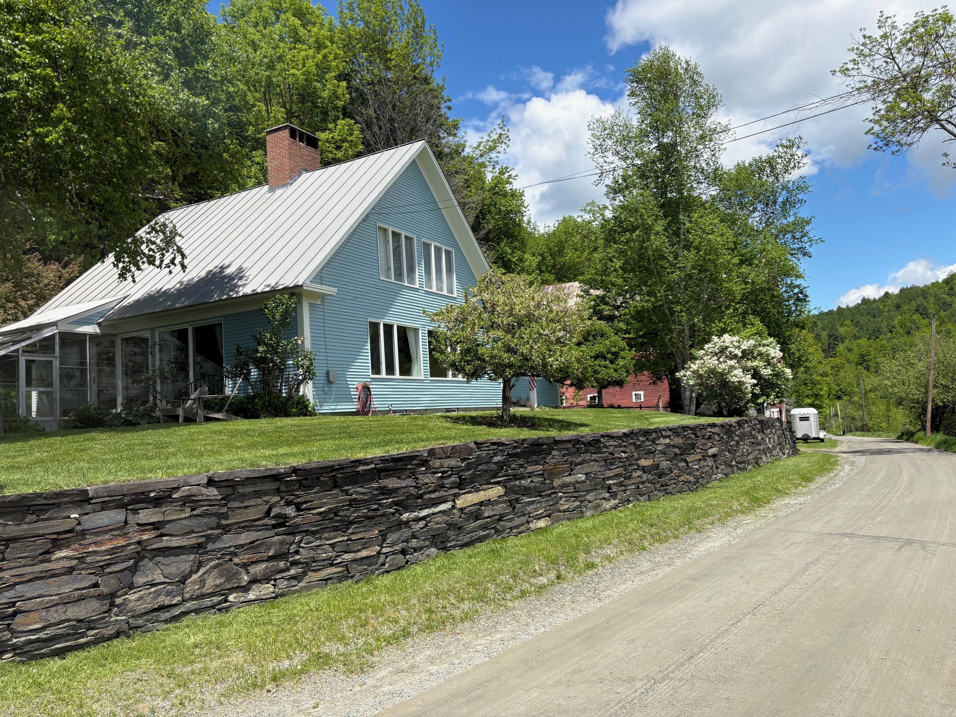 Une maison à deux étages avec un mur en pierre et un chemin de terre.