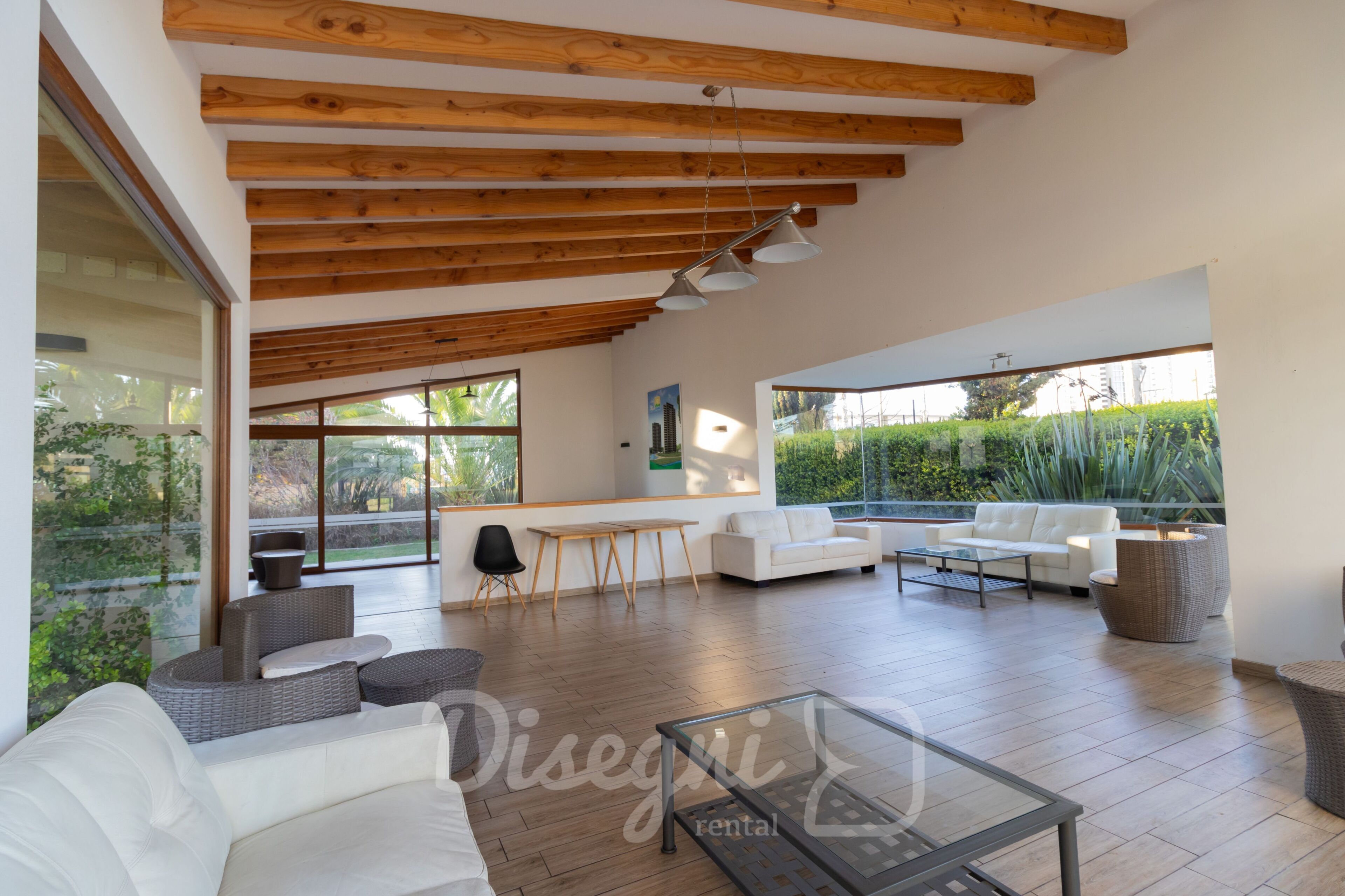 Amplia sala de estar con techo alto, vigas de madera y grandes ventanales con vistas a zonas verdes.
