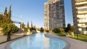 A swimming pool with a circular design, surrounded by a paved walkway, tall residential buildings, and greenery.