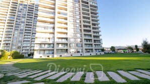 A modern high-rise building with multiple balconies, a well-maintained lawn, and a clear sky.