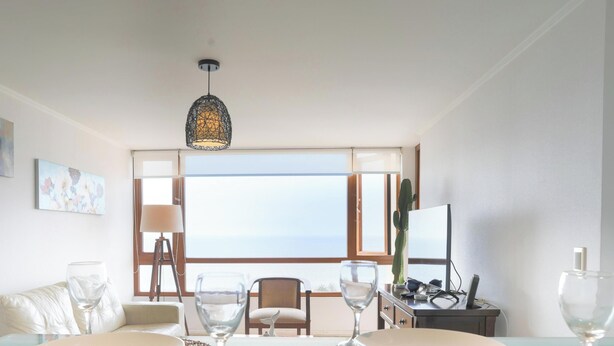 A room with a large window, a desk, a chair, a sofa, and a hanging light fixture.