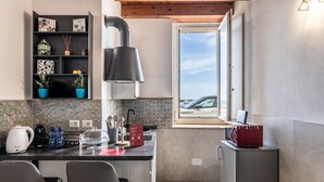 Eine kompakte Küche mit einer Kaffeestation, einem Fenster mit Ausblick und einer kleinen Schrank.