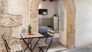 Ein steinerner Bogen führt in einen Raum mit einem Bett, einem an der Wand befestigten Fernseher und einem kleinen Tisch mit einer Topfpflanze.