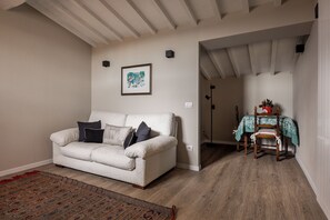 Ein Wohnzimmer mit Sofa, einem gemusterten Teppich, einem gerahmten Bild an der Wand und einem Essbereich mit Tisch und Stühlen.