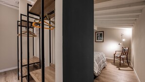 A bedroom with a bed, a chair, a wardrobe with hanging clothes, and a painting on the wall. - Libertà Heritage Residence by MMega (Florence)