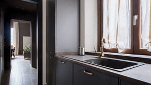 A modern kitchen with dark cabinetry, a stainless steel sink, and a window with sheer curtains. - Libertà Heritage Residence by MMega (Florence)