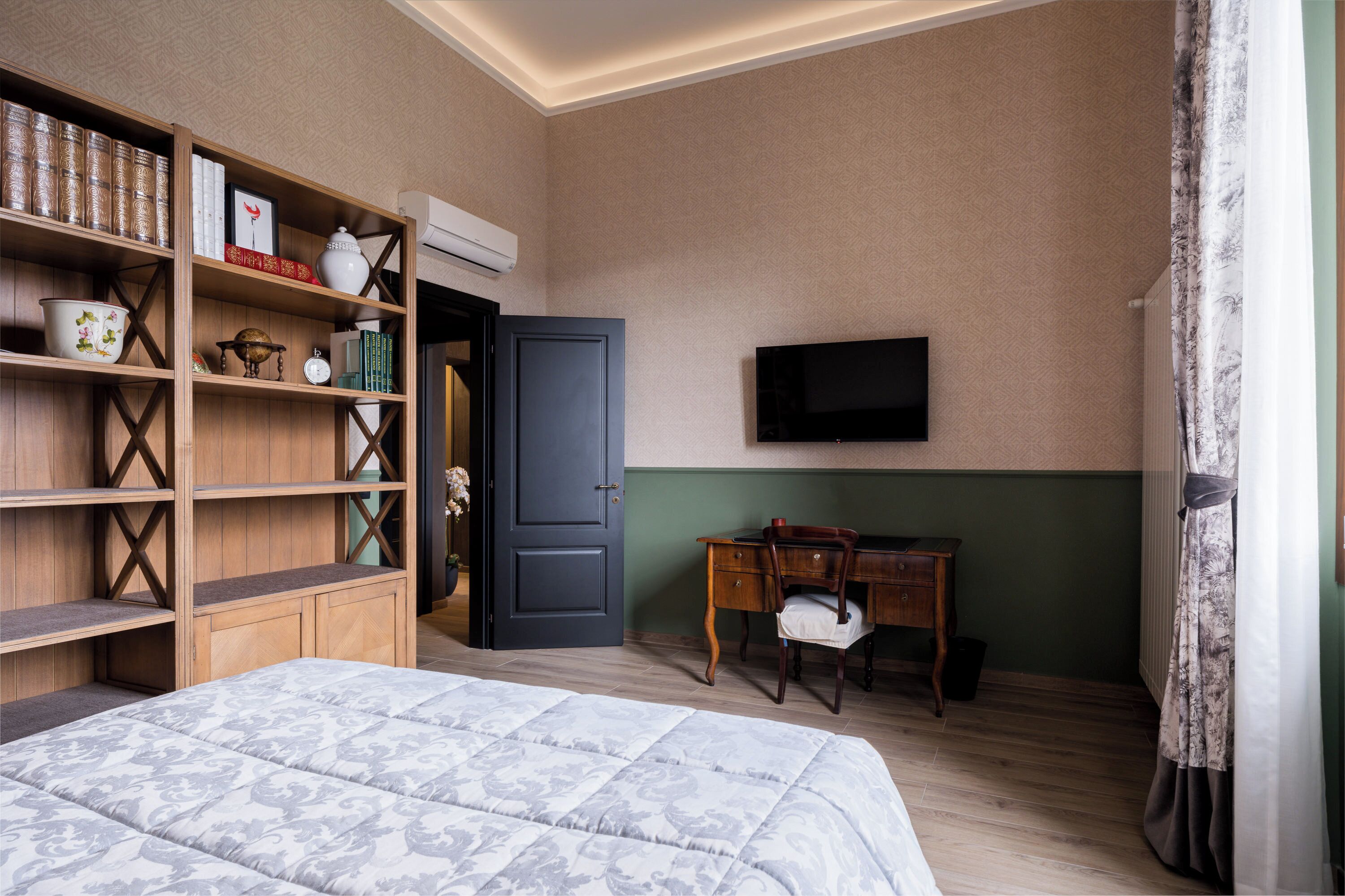 Ein Schlafzimmer mit einem Bett, einem Holzregal, einem Schreibtisch, einem Stuhl, einem Fernseher und einer Tür.