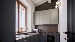 A modern kitchen with dark cabinetry, a built-in microwave, a gas stove, and a window with curtains. - Libertà Heritage Residence by MMega (Florence)