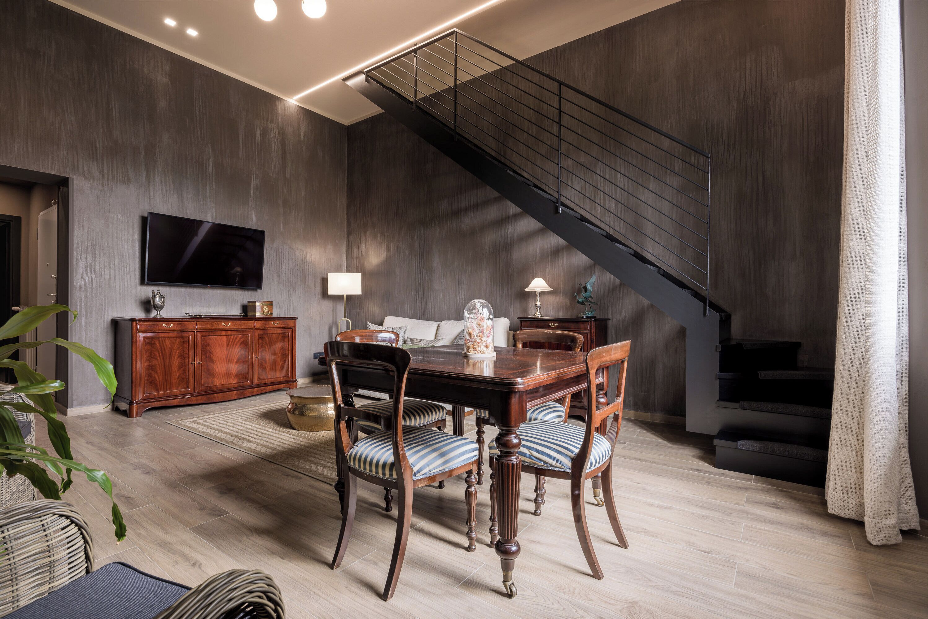 Ein Essbereich mit Holztisch und -stühlen, einem an der Wand montierten Fernseher und einer Treppe.