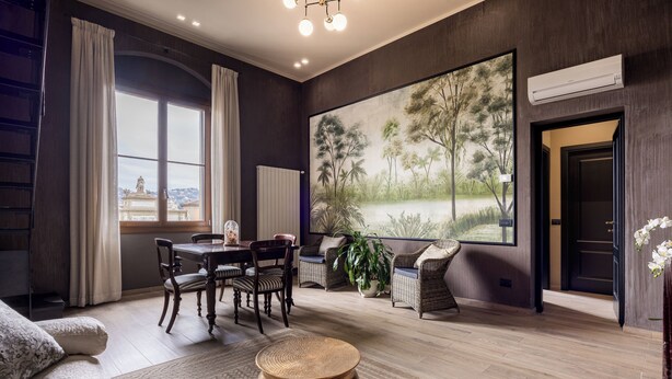 A modern living room with a dining area, a large painting, and a view of a cityscape through a window. - Libertà Heritage Residence by MMega (Florence)