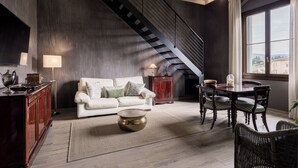 A modern living room with a staircase, a sofa, a dining table, and a view through a large window. - Libertà Heritage Residence by MMega (Florence)