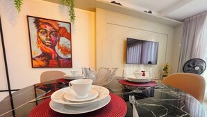 Un comedor con una mesa de vidrio, individuales rojos, platos blancos y un cuadro en la pared.