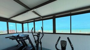 Un gimnasio con equipo de ejercicio y amplias ventanas que ofrecen vistas a la playa y al océano.