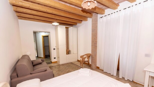 Een hotelkamer met een bed, een bank, een stoel, een houten plafond en een bakstenen muur.