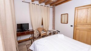 Een slaapkamer met een bed, een televisie, een bureau, een stoel en een houten deur.