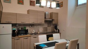 A compact kitchen with wooden cabinets, a microwave, a kettle, and a dining table with chairs. - Happy feelings in Florence (Firenze)