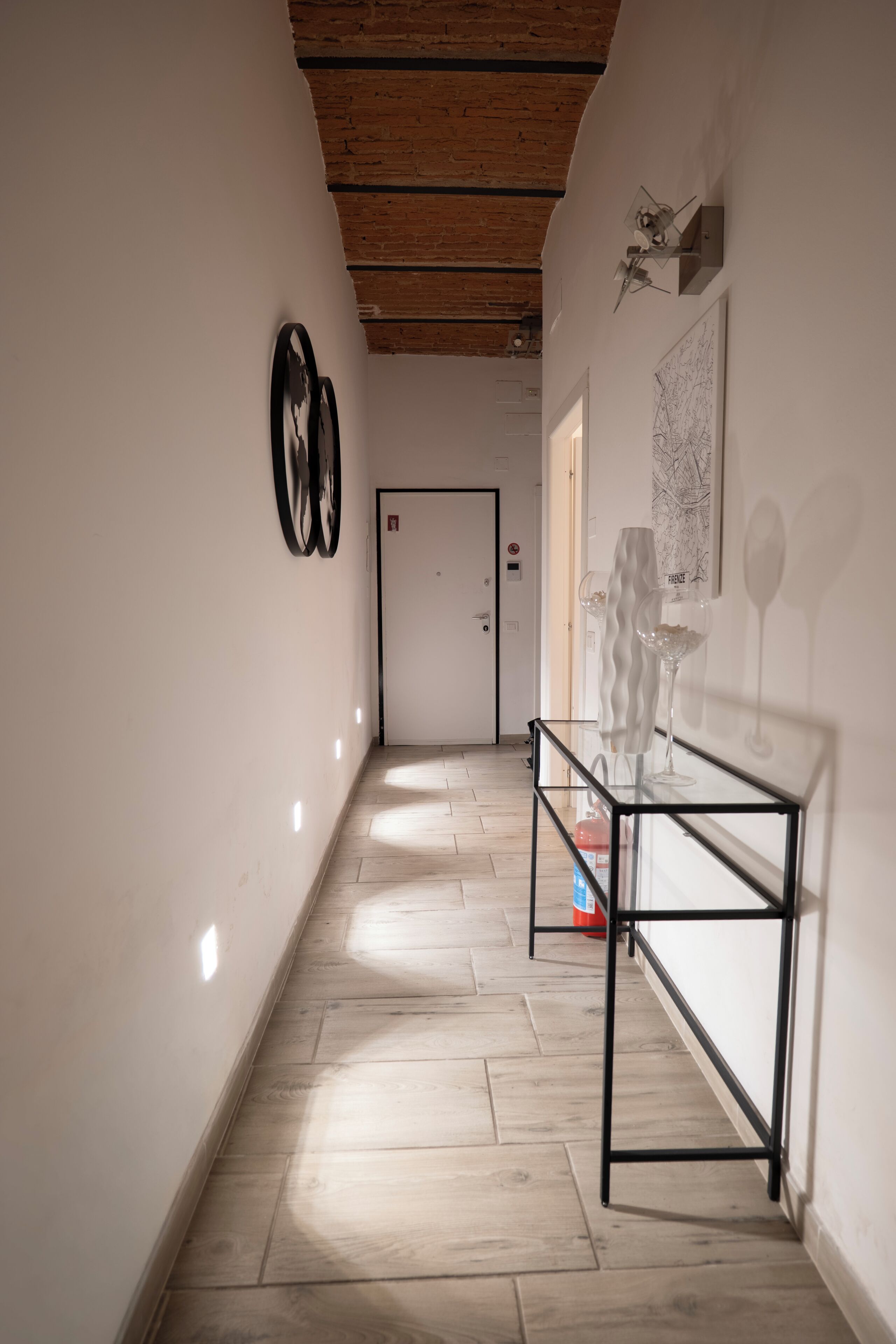 Un couloir avec un plafond en bois, une table en verre ornée d’objets décoratifs et une porte au fond.