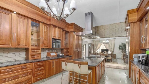 Eine geräumige Küche mit Holzschränken, einer zentralen Kochinsel mit Barhocker und einem modernen Kronleuchter.