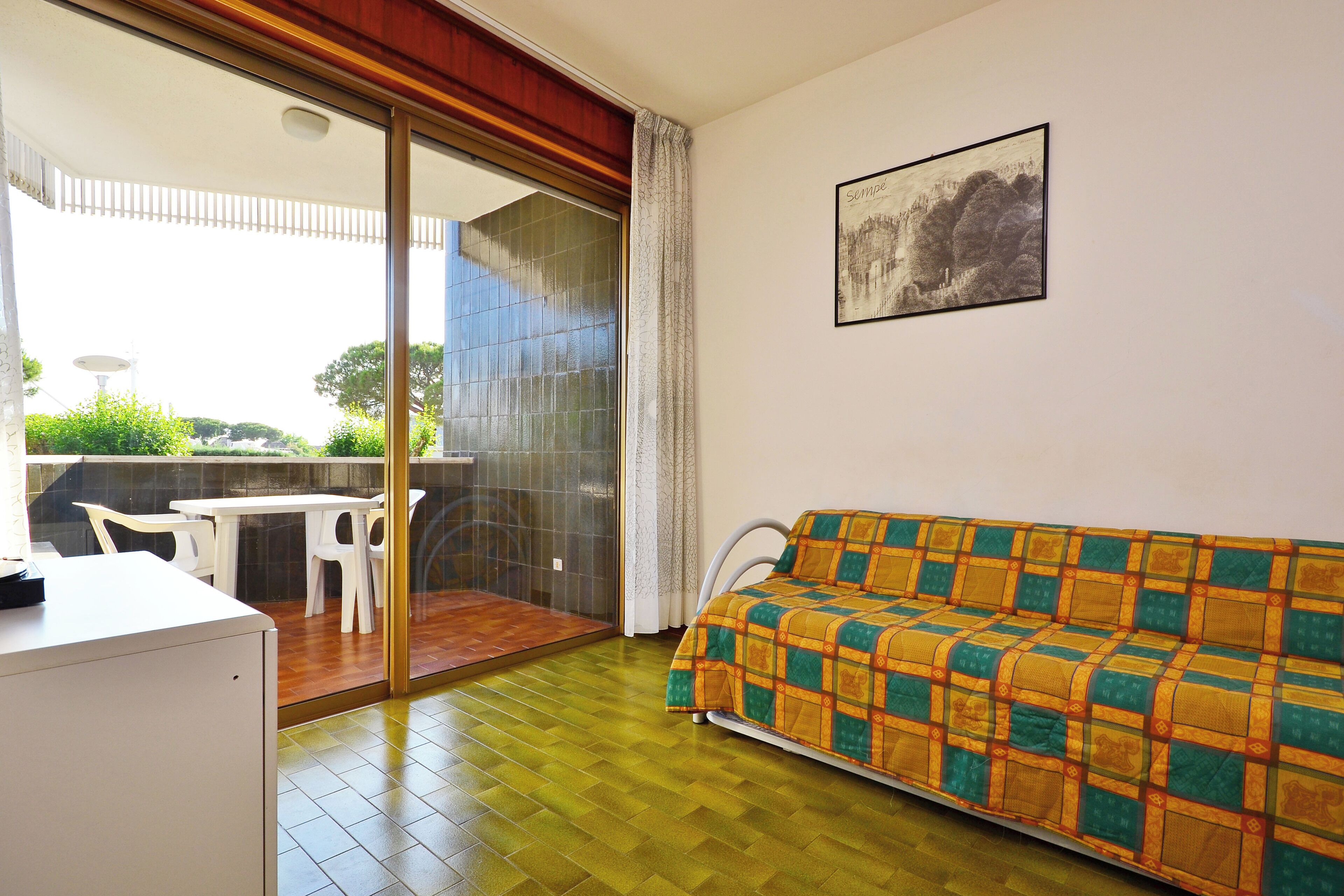 Habitación con sofá, escritorio y puerta de vidrio que da a un área exterior con mesa y sillas.