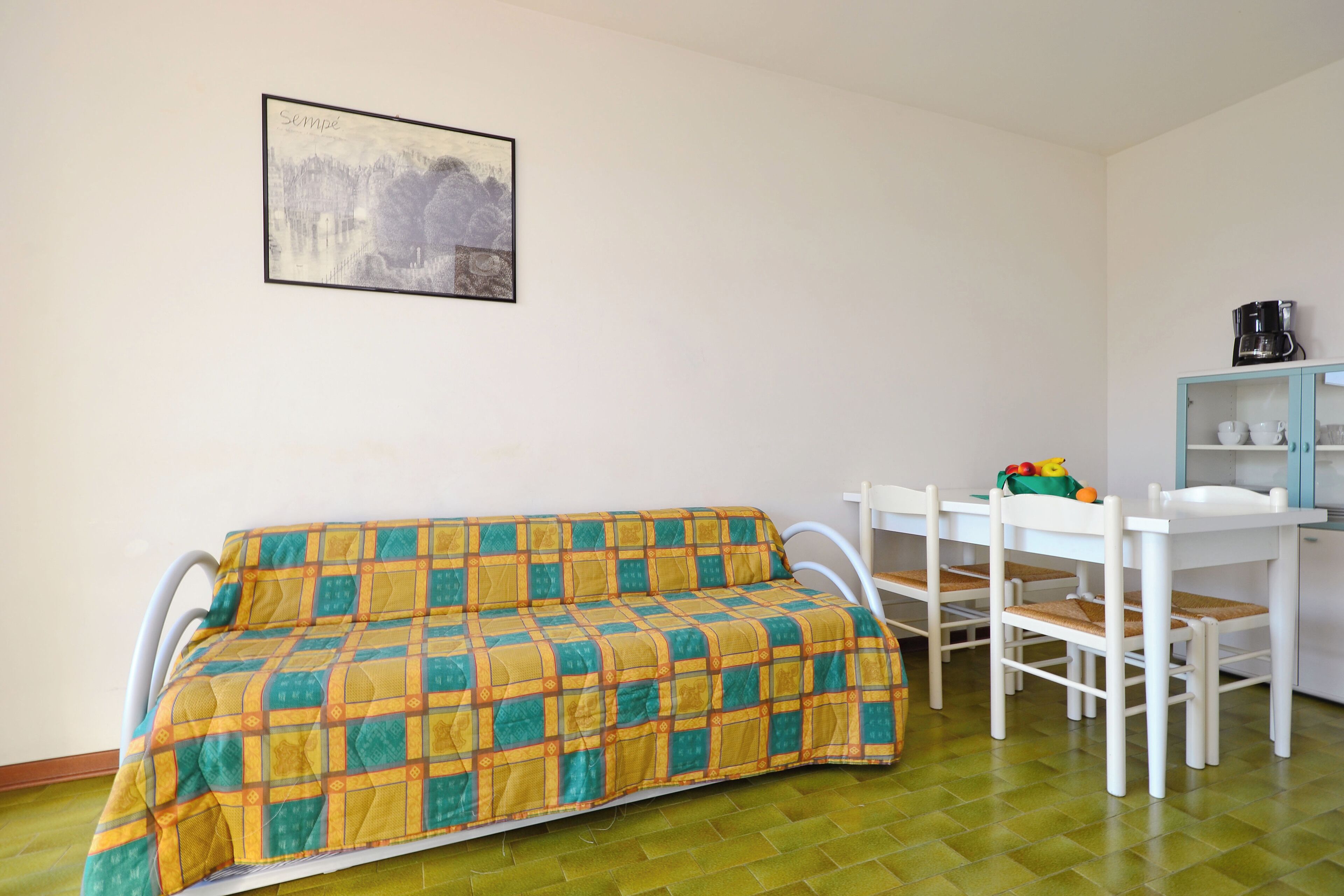 Une pièce comprenant un lit, une table, des chaises, une machine à café et un tableau encadré accroché au mur.