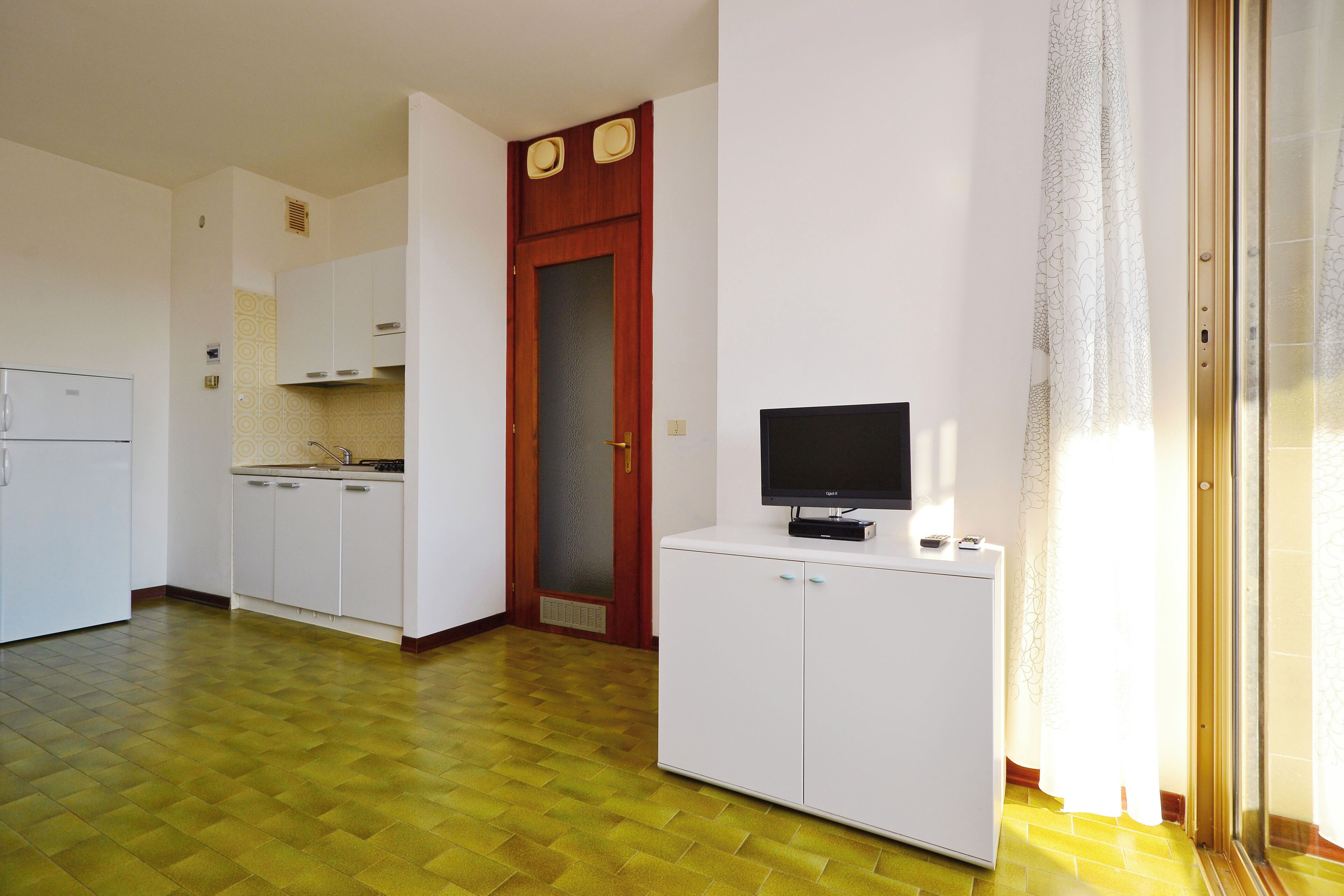 A kitchen with white cabinets, a refrigerator, and a television on a white cabinet.