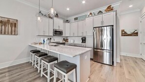 Een moderne keuken met witte kasten, een roestvrijstalen koelkast en een marmeren kookeiland met barstoelen.