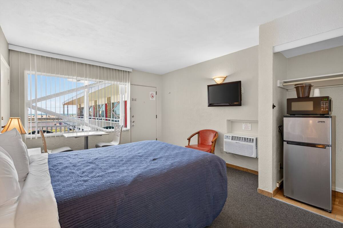 Une chambre d’hôtel équipée d’un lit, d’une télévision, d’un four à micro-ondes, d’une chaise et d’une fenêtre donnant sur des immeubles.
