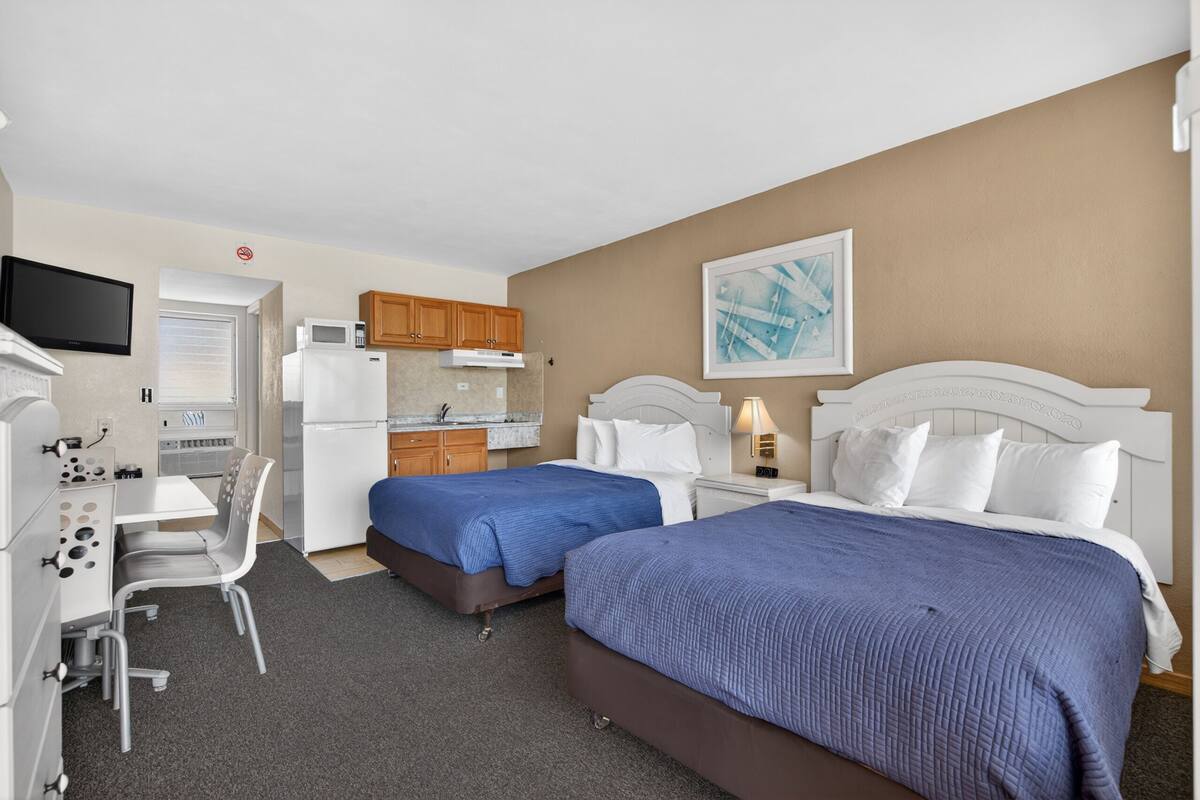 Une chambre d’hôtel avec deux lits, un bureau, une chaise, un four à micro-ondes, un réfrigérateur et une télévision.