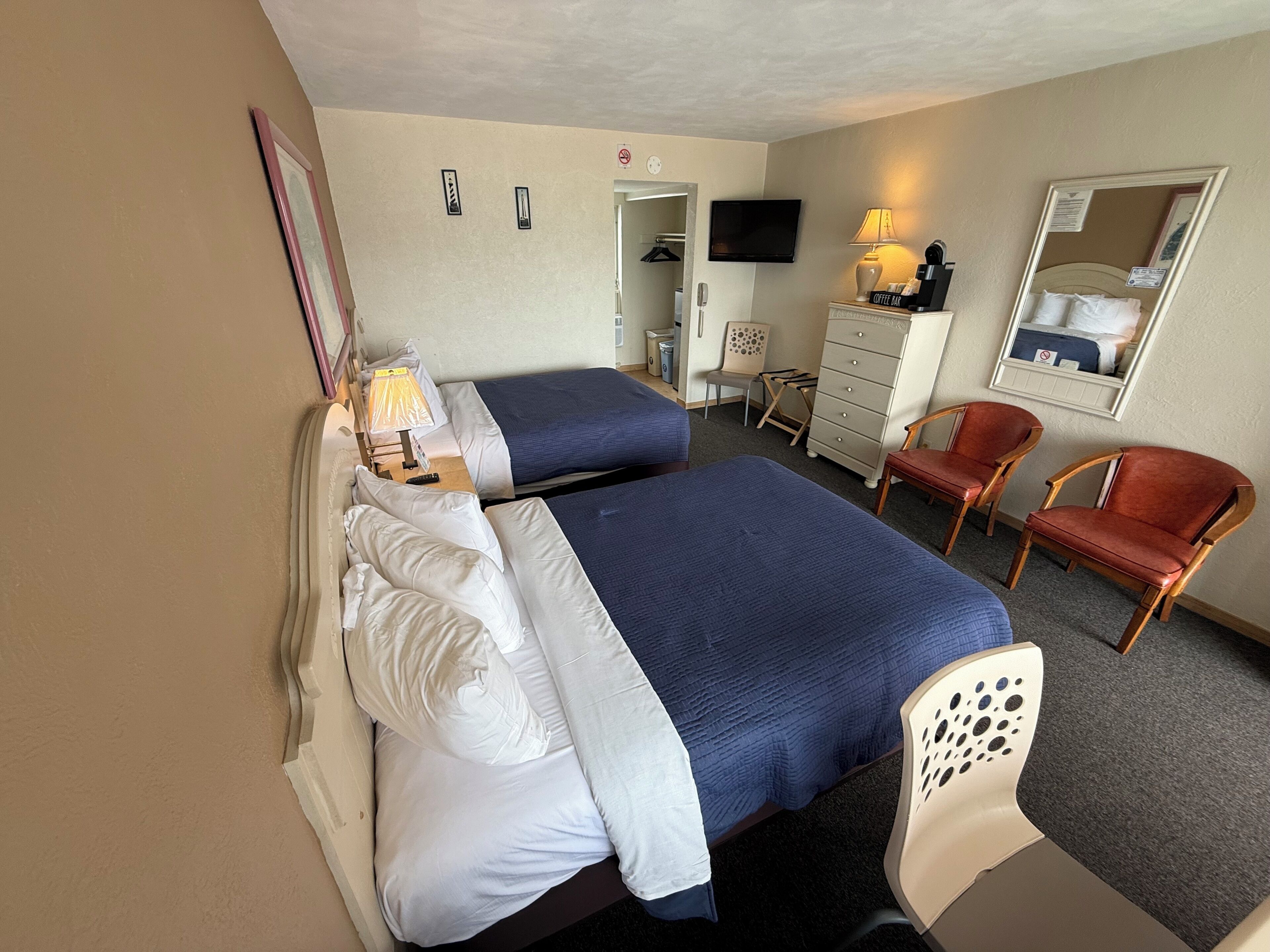 A hotel room with two beds, a TV, a coffee maker, a chair, and a dresser.