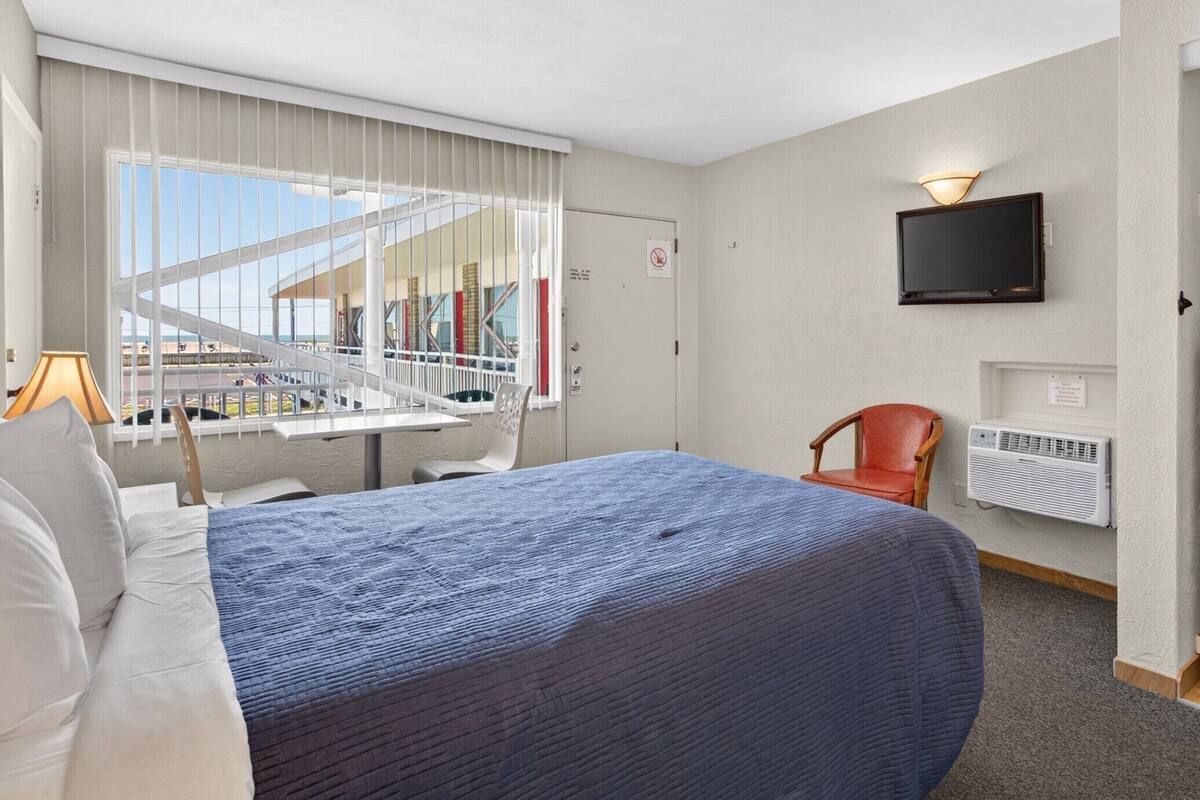 Une chambre d’hôtel avec un lit, une chaise, une télévision et une fenêtre donnant sur un immeuble.