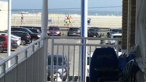 Uitzicht op een parkeerplaats met meerdere auto's, een strand op de achtergrond en een metalen hek in de voorgrond.
