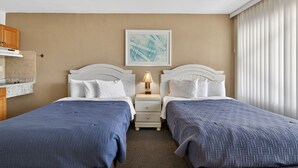 Een hotelkamer met twee bedden, een nachtkastje met een lamp, een inlijsting foto aan de muur en een raam met jaloezieën.