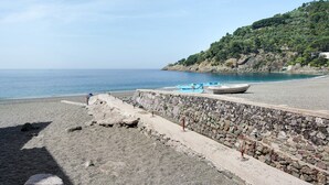 Una spiaggia con un muro di pietra, una barca e un pendio roccioso.