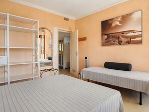 Une chambre avec deux lits, une armoire, un miroir et un tableau représentant une scène de plage.