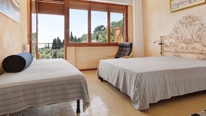 Una stanza con due letti, una sedia, una finestra vista sul verde e un quadro appeso al muro.