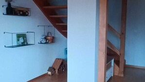 A room with a wooden staircase, a white wall, and a small table with a vase.