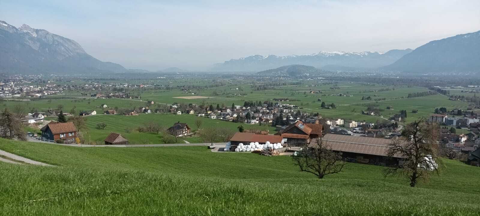A rural landscape with houses, a road, and mountains in the background.