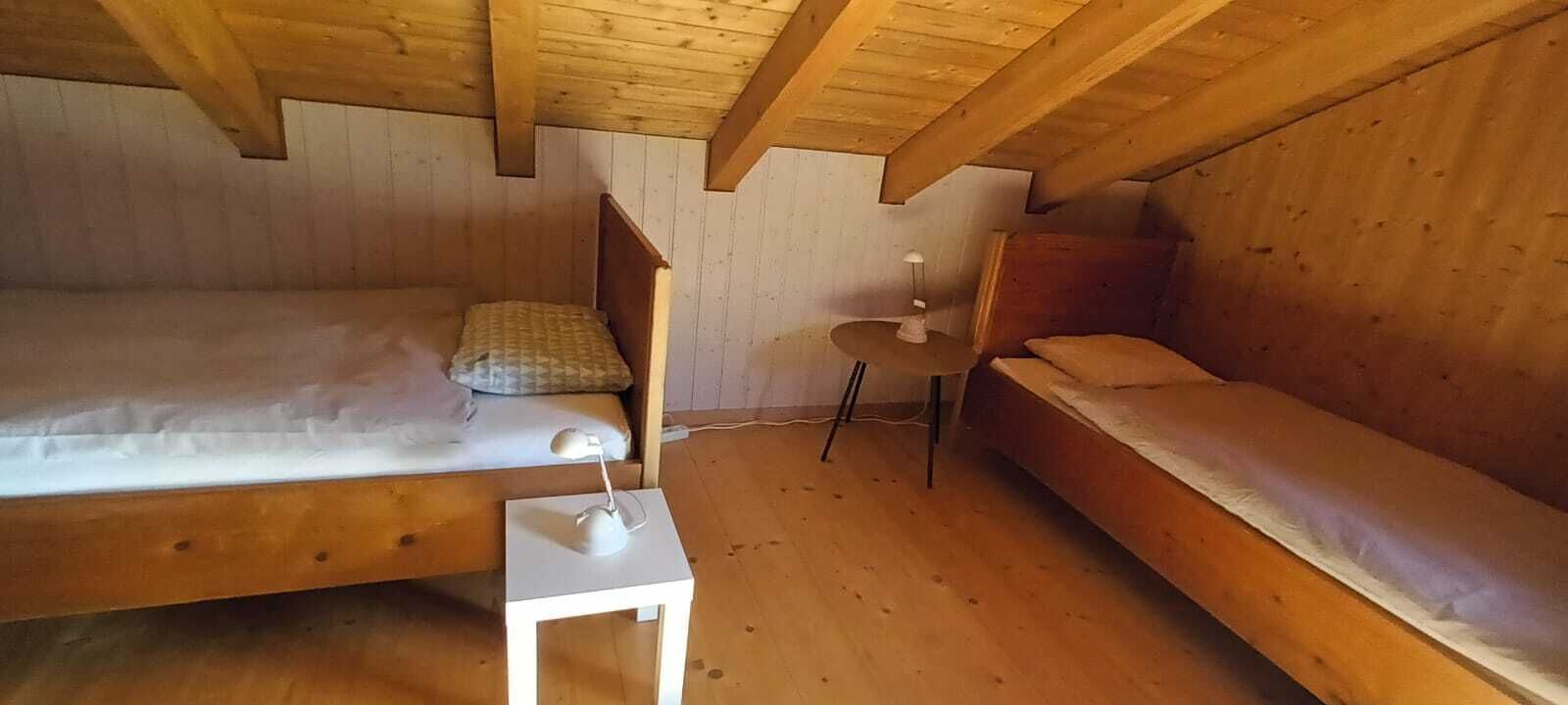 Een houten kamer met twee bedden, een klein wit tafeltje met een lamp en een plafondventilator.