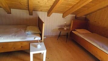 Een houten kamer met twee bedden, een klein wit tafeltje met een lamp en een plafondventilator.