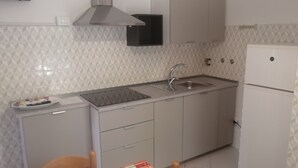 Eine kompakte Küche mit eingebautem Herd, Spüle und Kühlschrank. Es gibt Schränke und eine Arbeitsplatte.