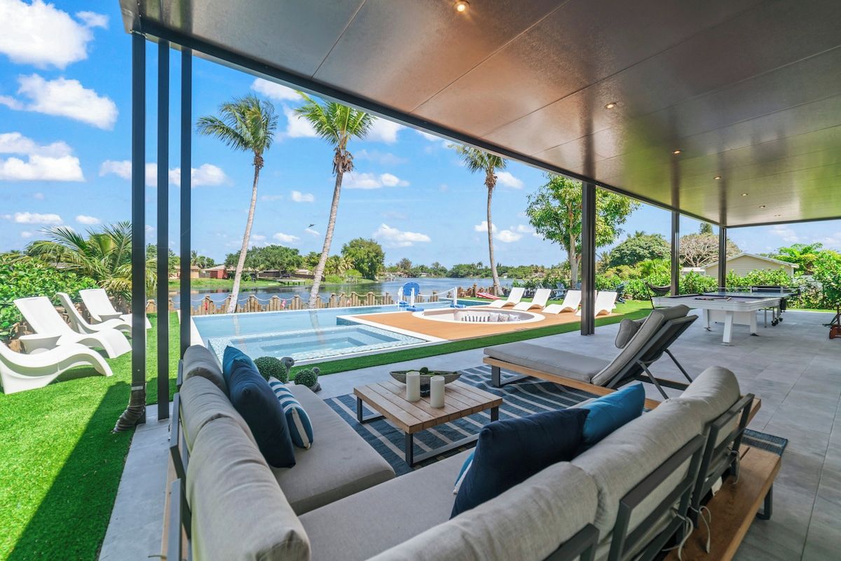 A modern outdoor lounge area with a pool, sun loungers, and a view of the surrounding landscape.