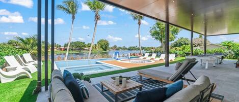 A modern outdoor lounge area with a pool, sun loungers, and a view of the surrounding landscape.
