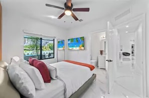 Une chambre d’hôtel moderne équipée d’un lit, d’un ventilateur de plafond, d’une grande fenêtre donnant sur une piscine et d’une porte menant à la salle de bain.