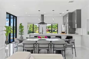Une cuisine moderne dotée d’un îlot central, de grandes fenêtres et offrant une vue sur la verdure.