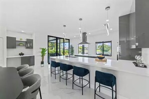 Una cocina moderna con una isla central, taburetes de bar y vistas al exterior.