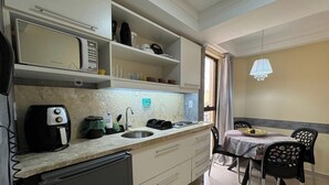 A compact kitchen with a microwave, coffee maker, and a sink. There is a dining area with a table and chairs. - Mardisa Flat - Miramar Hospedagens  (João Pessoa)